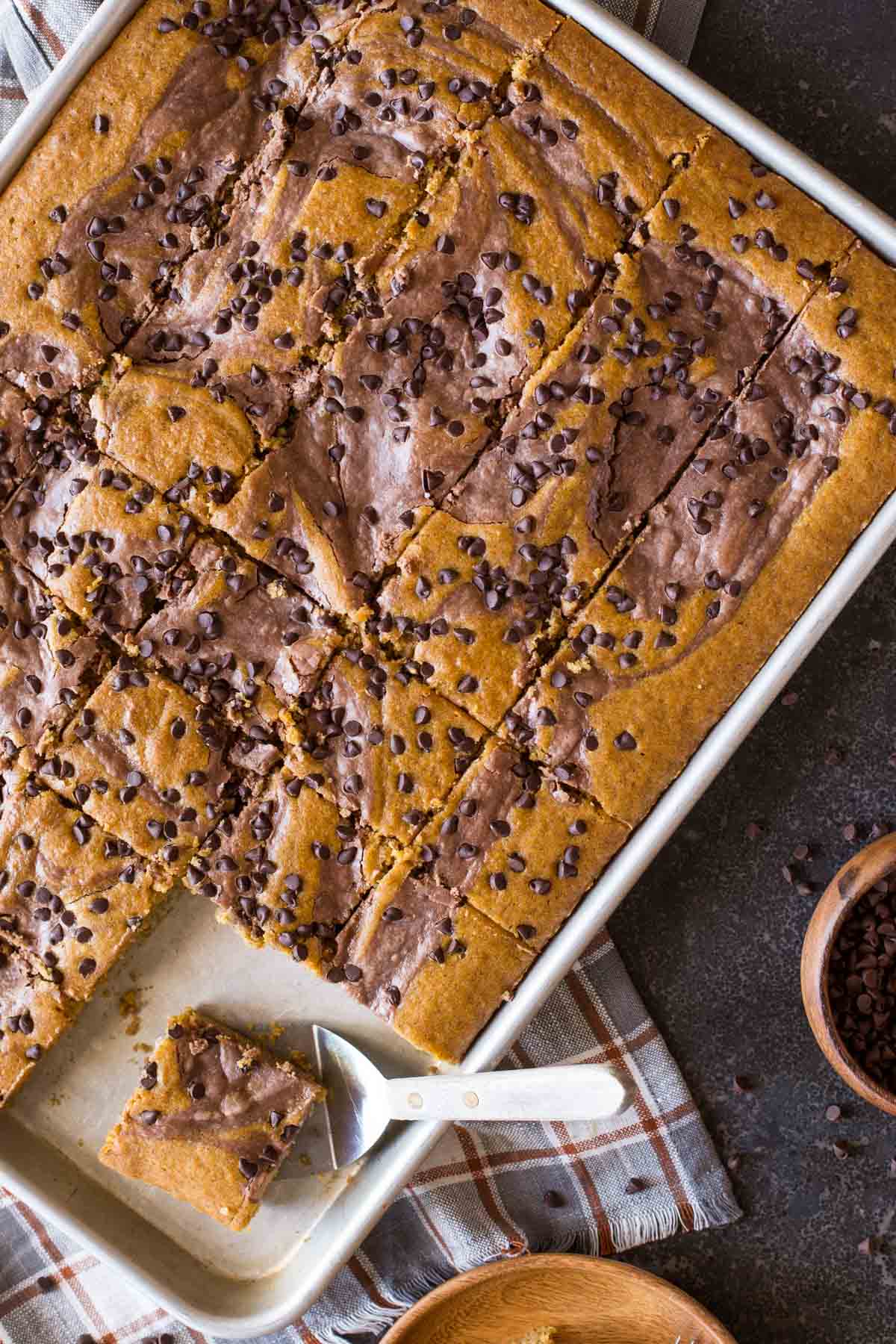 Chocolate-Swirled Pumpkin Bars cut in a baking pan with a serving spatula under one of the bars.