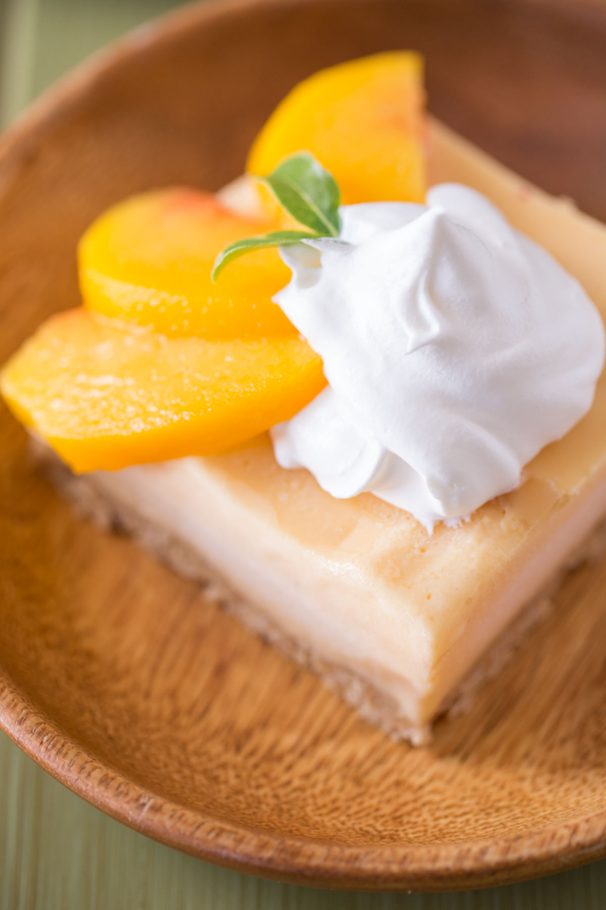 An Easy Homemade Peach Ice Cream Bar on a wood plate, topped with whipped cream and fresh peach slices. 