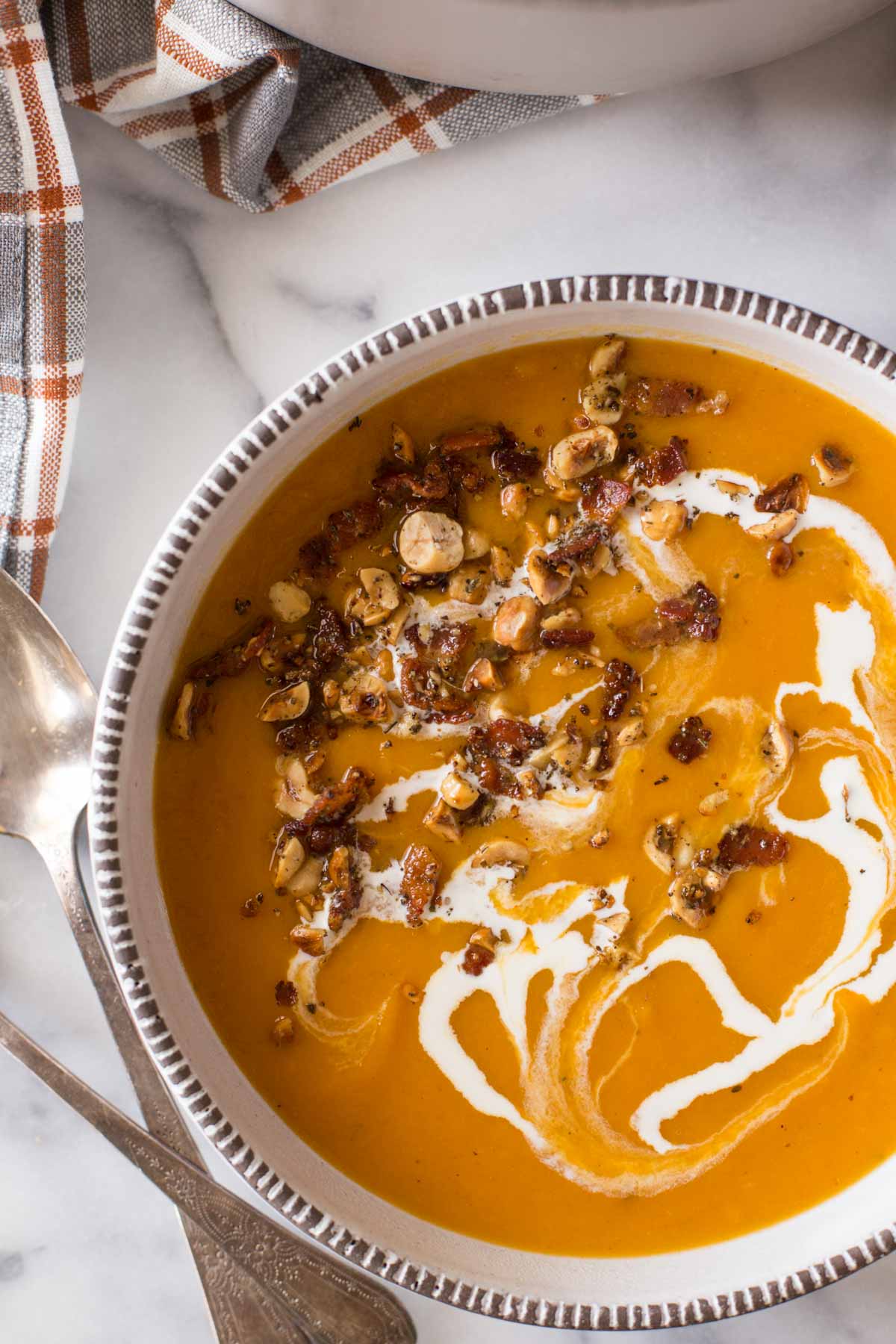 Roasted Butternut Squash Soup in a bowl with a swirl of heavy cream, and topped with a sprinkle of bacon and hazelnuts.