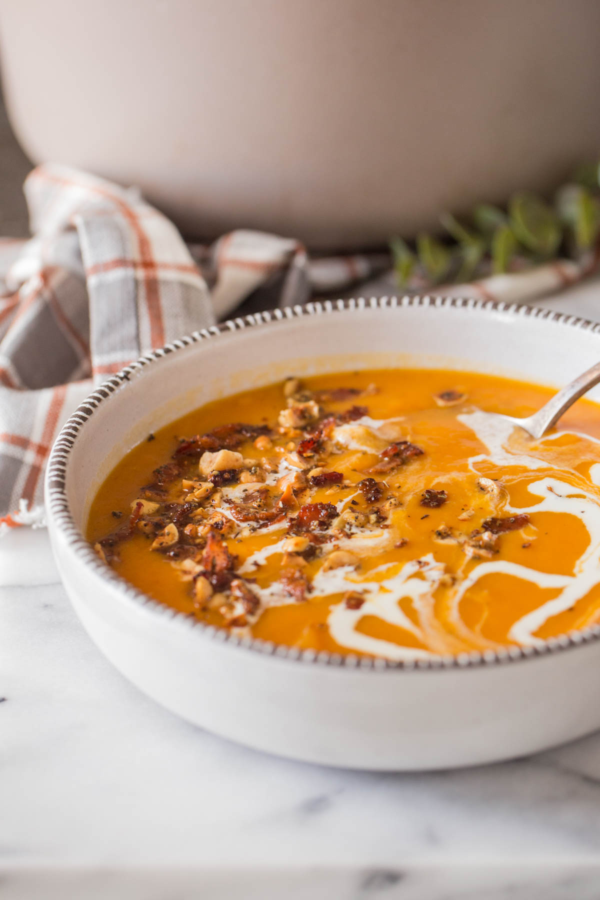 Roasted Butternut Squash Soup in a bowl with a swirl of heavy cream, and topped with a sprinkle of bacon and hazelnuts.