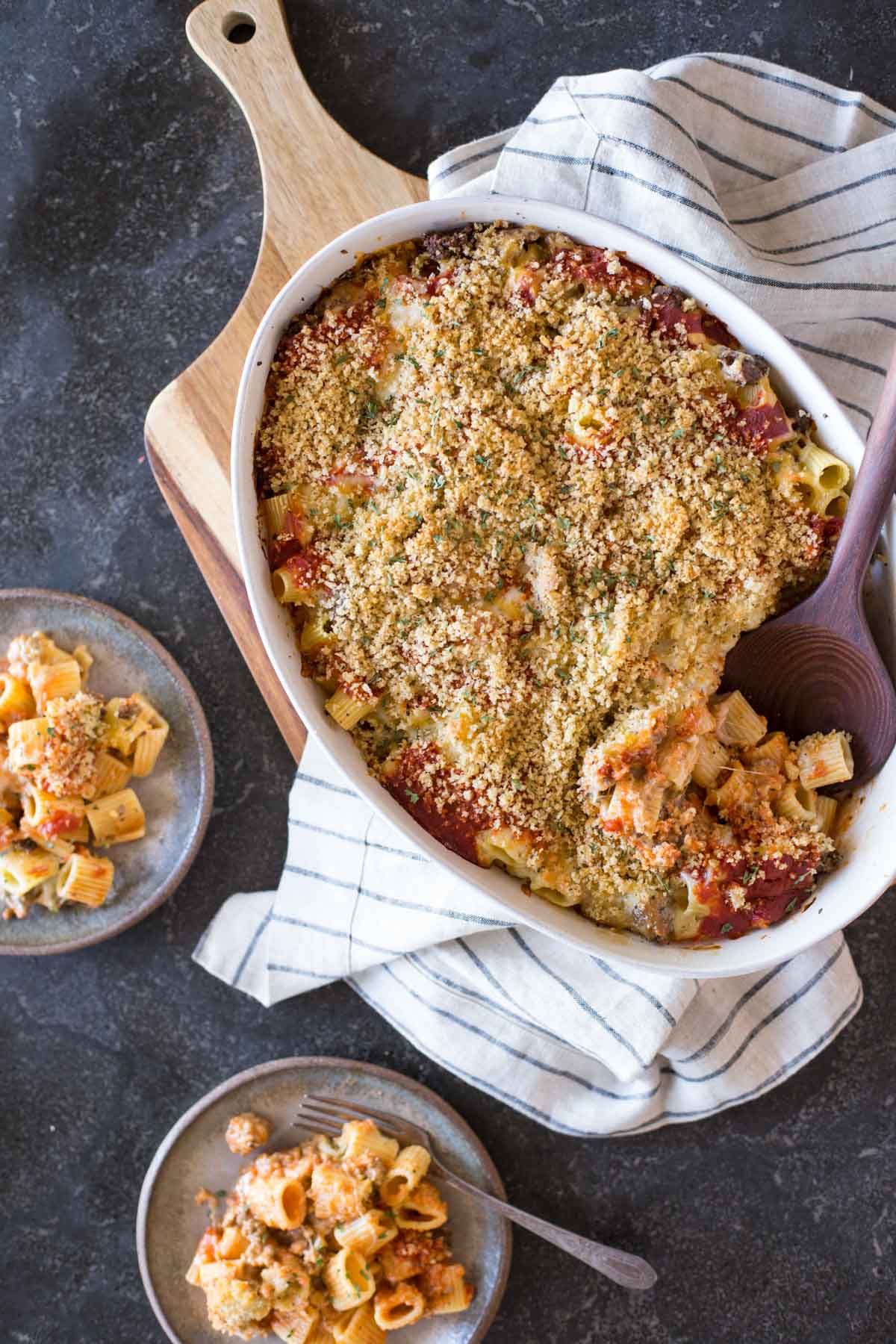 Cheesy Tomato Alfredo Pasta Bake in a baking dish with a serving spoon in it, with two plates of the Cheesy Tomato Alfredo Pasta Bake next to it.  