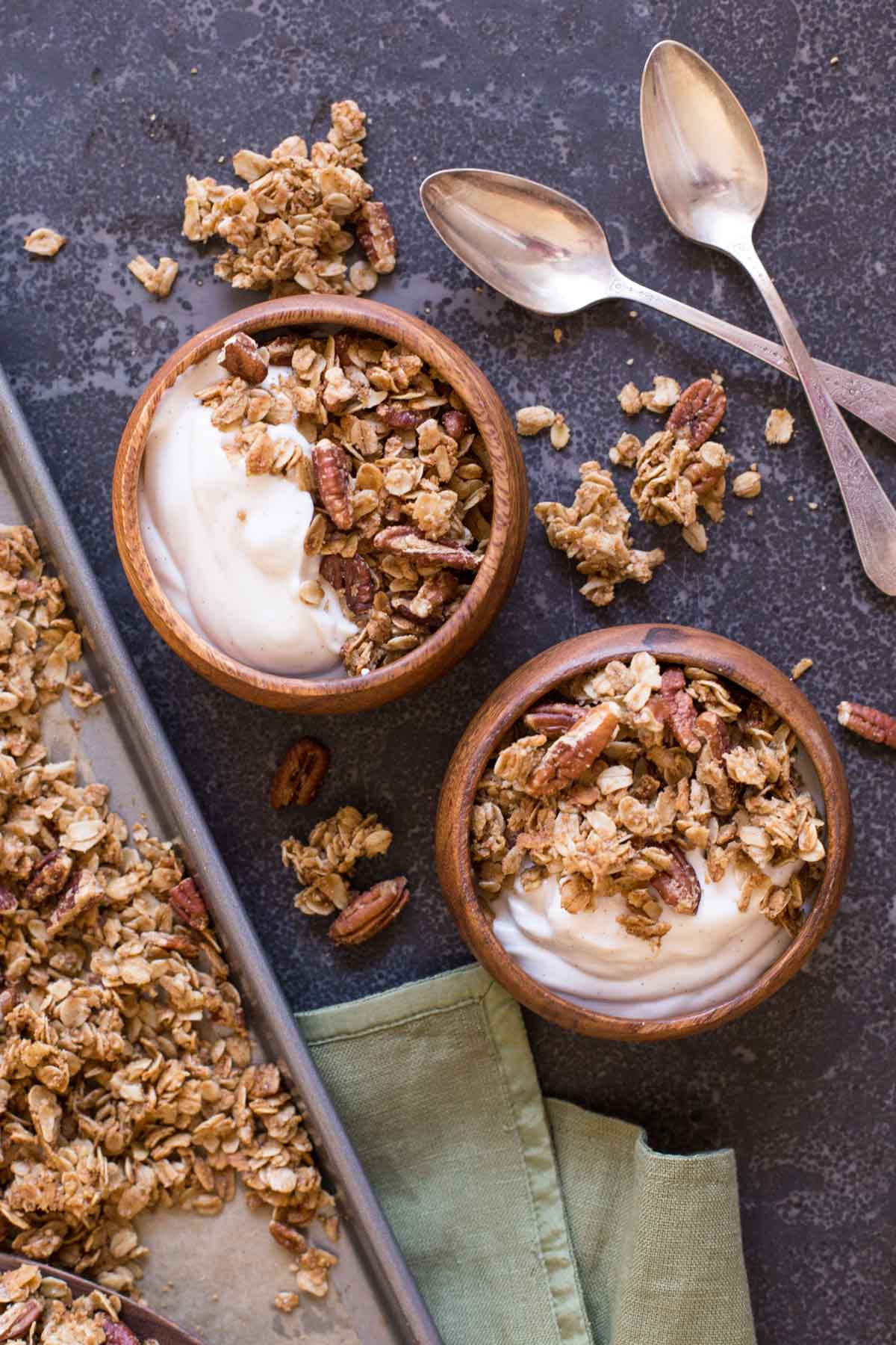 Two bowls of yogurt and Gingerbread Spice Granola, with two spoons next to them.  