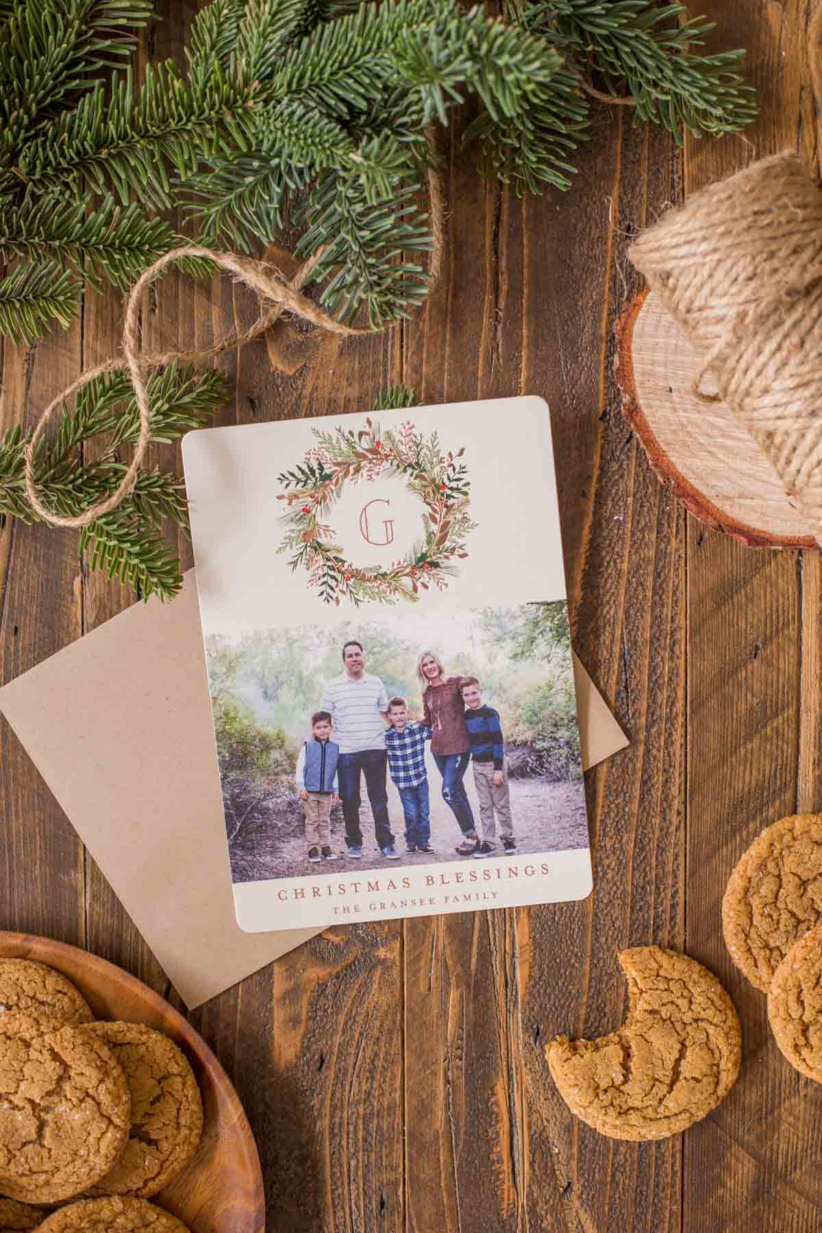 A Christmas Card that is sitting next to a plate of Old Fashioned Ginger Snaps, and some more Old Fashioned Ginger Snaps on the other side of the card, with a bite taken out of one of them. 