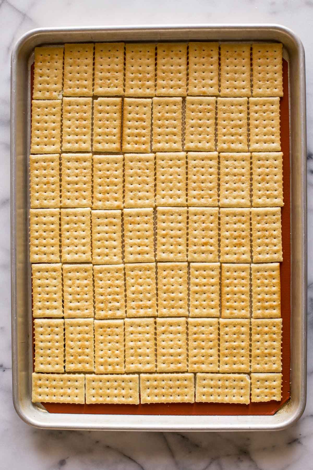 A Silpat lined, rimmed baking sheet with butter crackers arranged in a single layer for the base of the Take Five Cracker Bark.