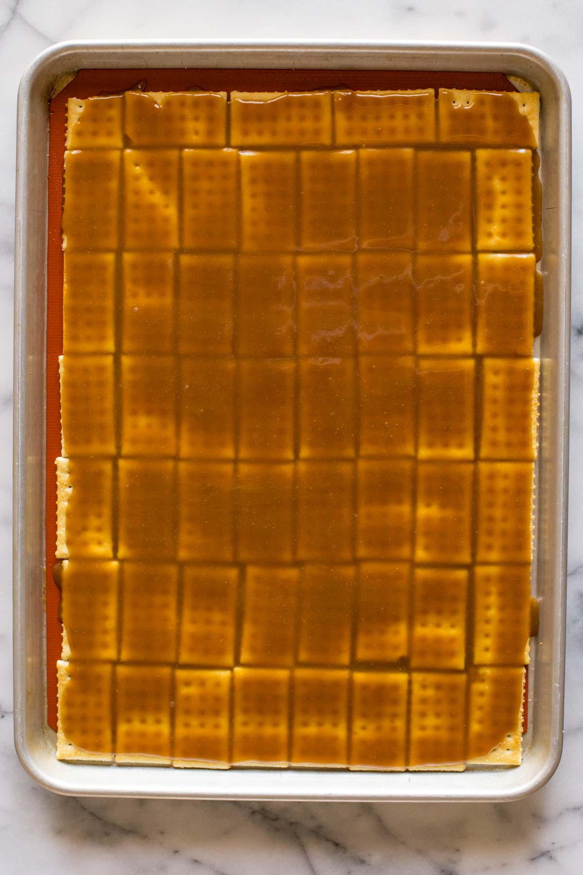 A Silpat lined, rimmed baking sheet with butter crackers arranged in a single layer with the caramel mixture poured on top of them. 