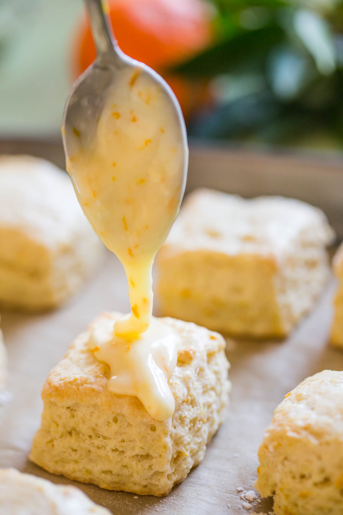 Mini Orange Cream Scones on a parchment paper lined baking sheet, being topped with orange icing.  