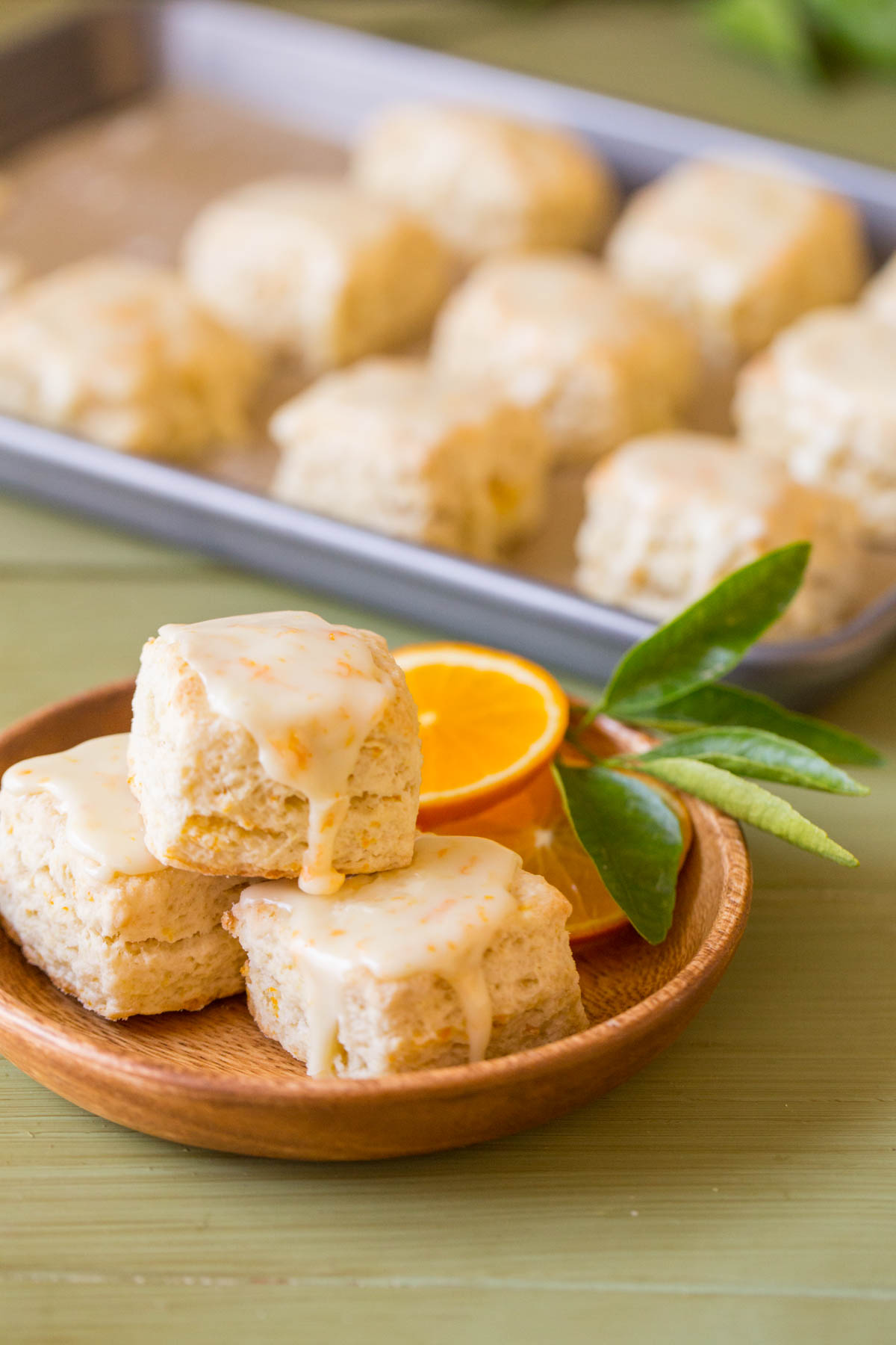 Mini Orange Cream Scones stacked on a small wood plate, with the baking sheet of Mini Orange Cream Scones in the background.