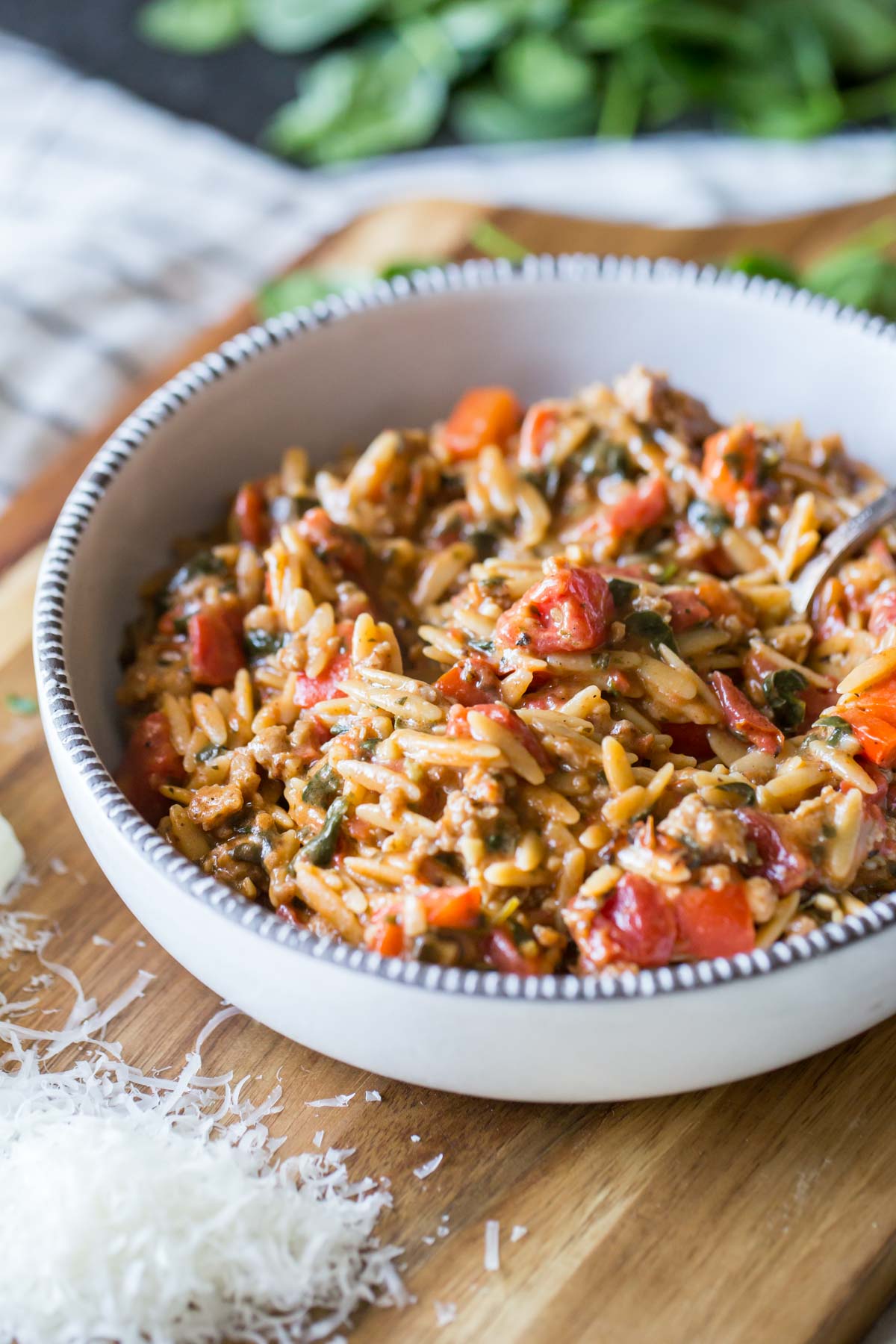 One Pot Creamy Tomato Orzo in a bowl, sitting on a board with some freshly grated parmesan cheese and some baby spinach. 