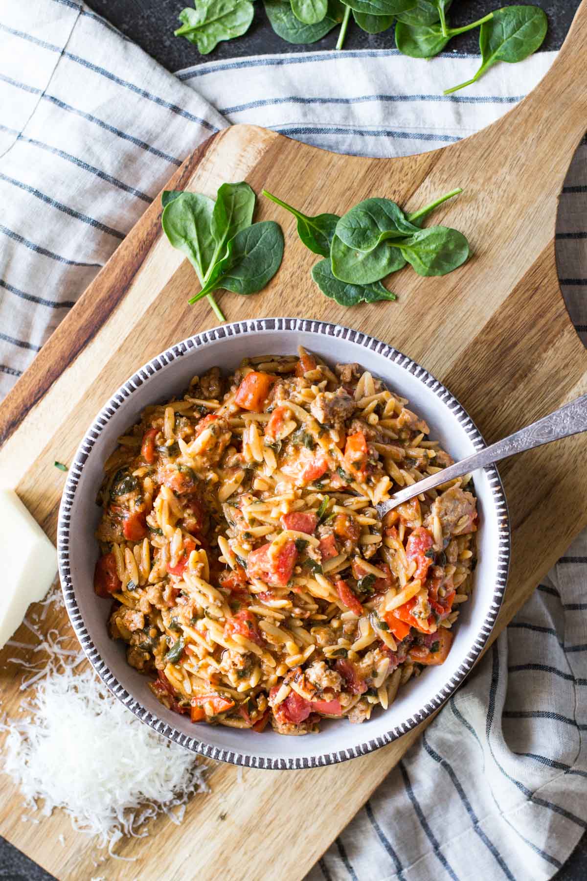 One Pot Creamy Tomato Orzo in a bowl, sitting on a board with some freshly grated parmesan cheese and some baby spinach. 