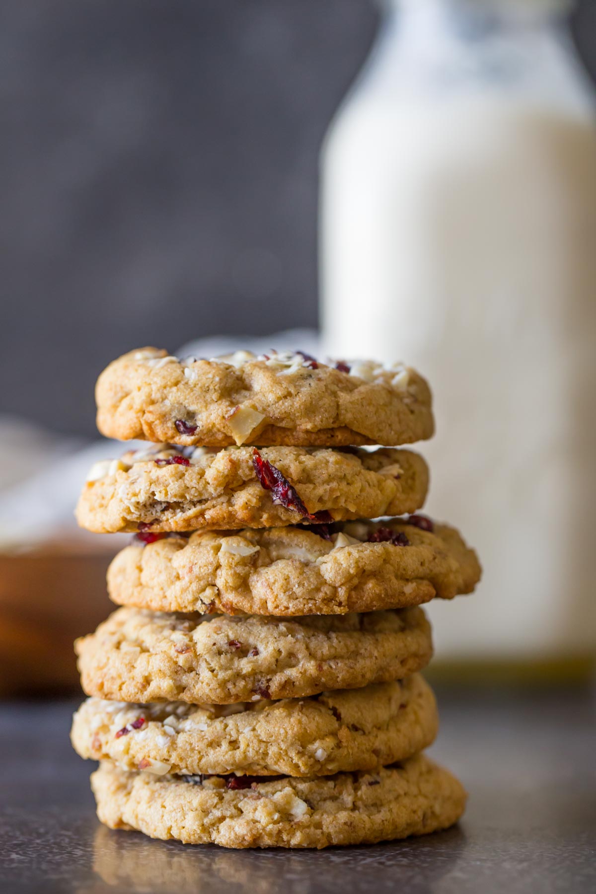 Cranberry Almond White Chocolate Chunk Cookies stacked in a pile of six, with a glass jar of milk in the background. 