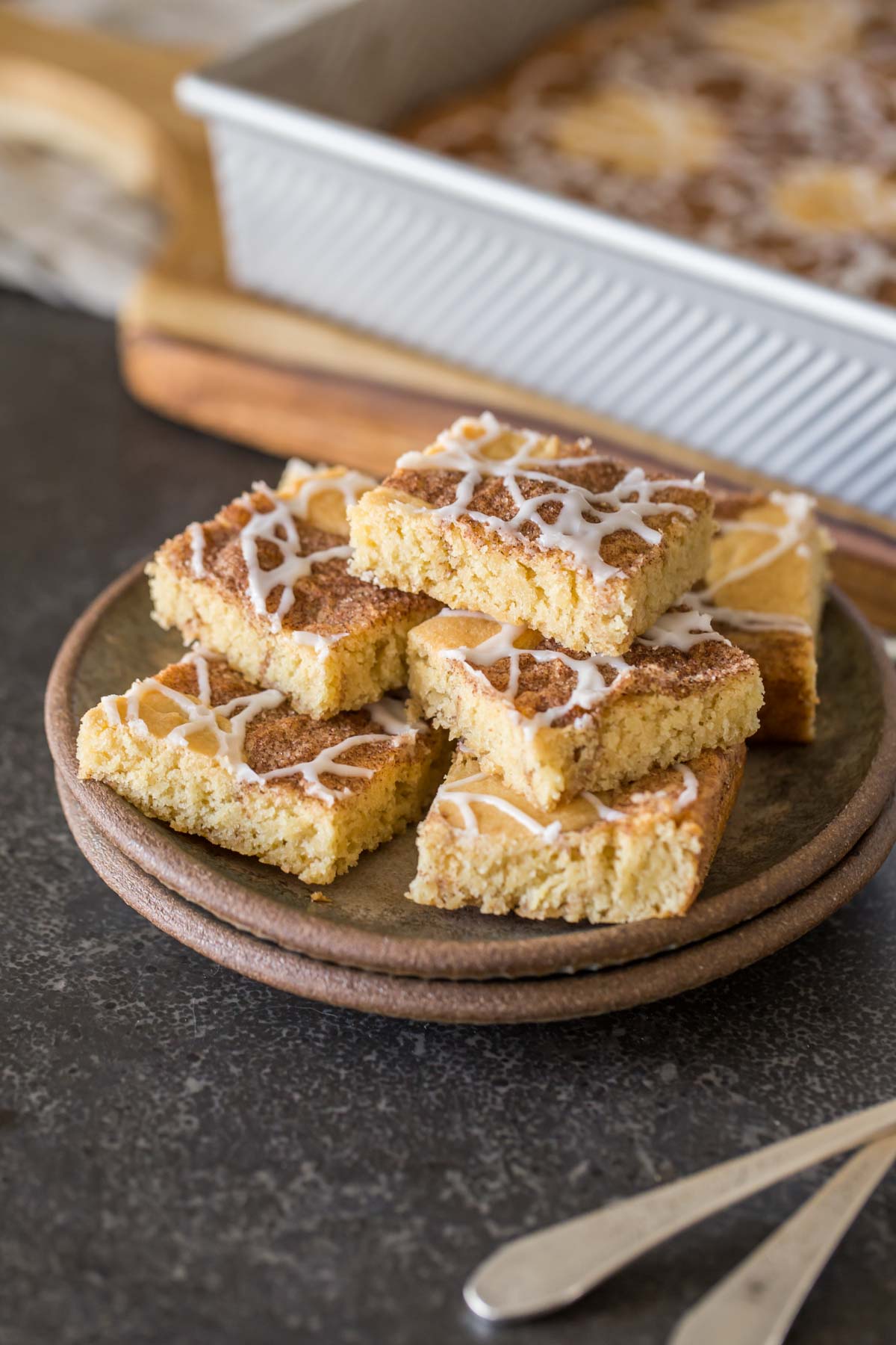 Snickerdoodle Bars stacked on a plate, with the baking dish of the rest of the Snickerdoodle Bars in the background. 