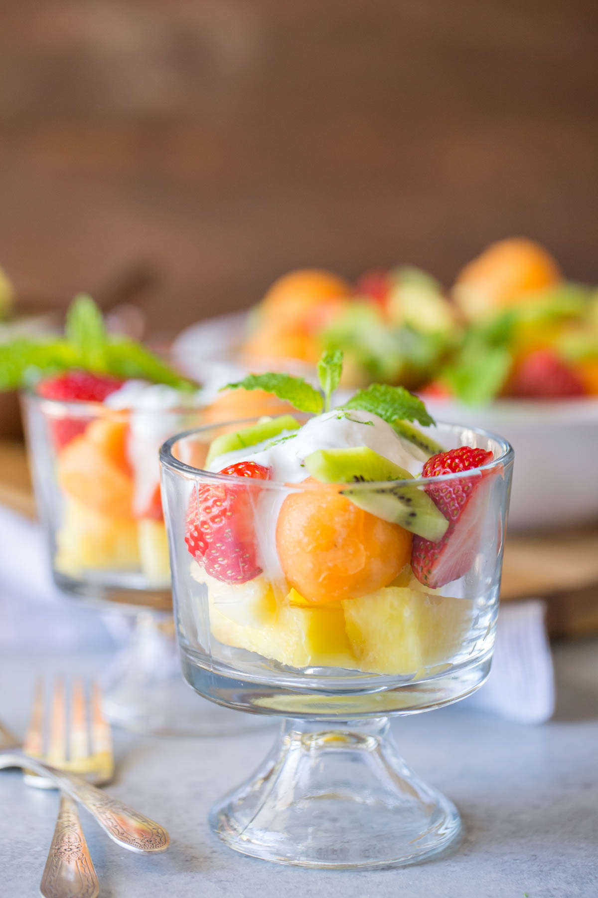 Summer Fruit Salad in a glass dish, topped with Coconut Lime Yogurt and mint leaves.  
