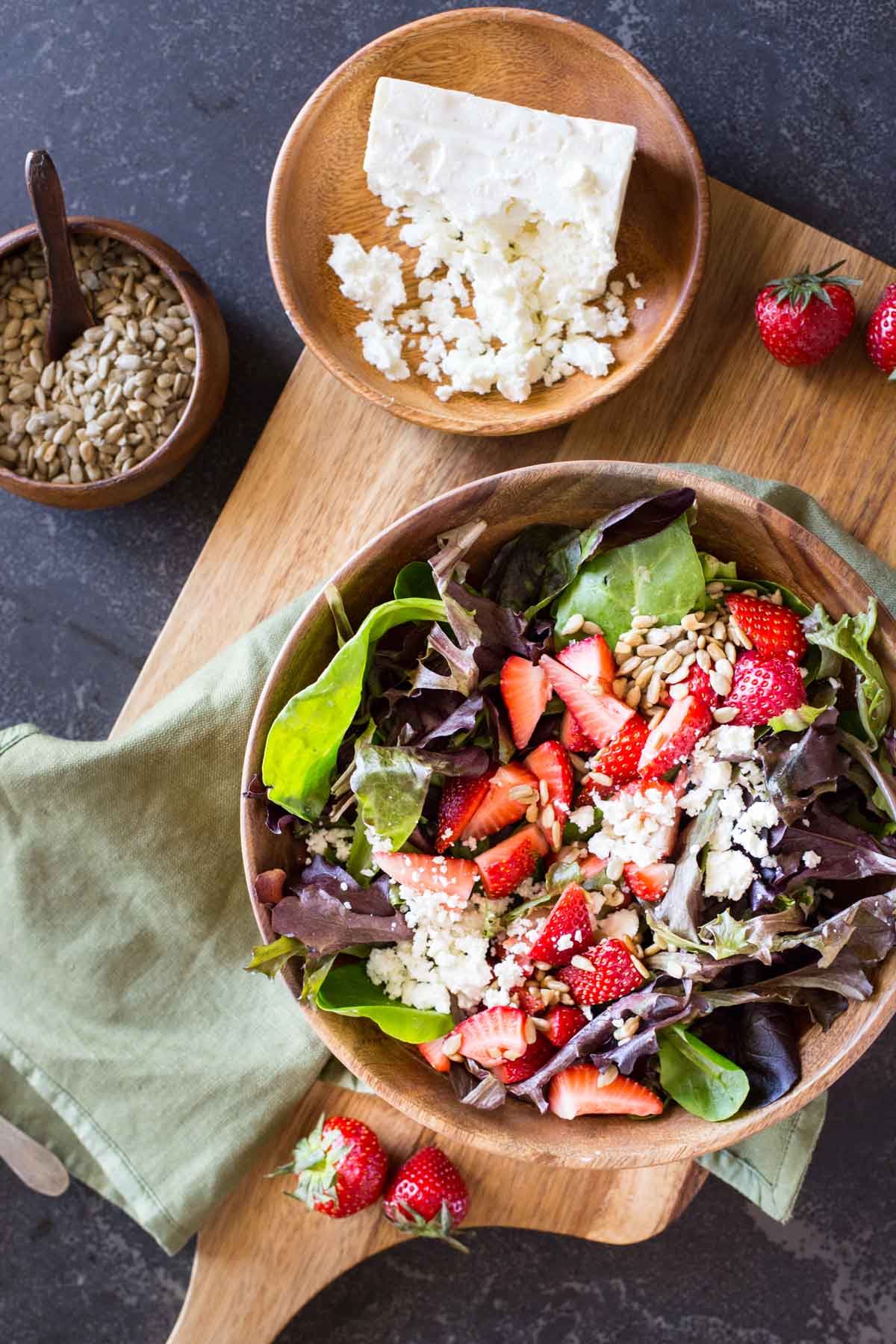 A bowl of Easy Strawberry Balsamic Salad sitting next to a small bowl of crumbled feta and a small bowl of sunflower seeds. 