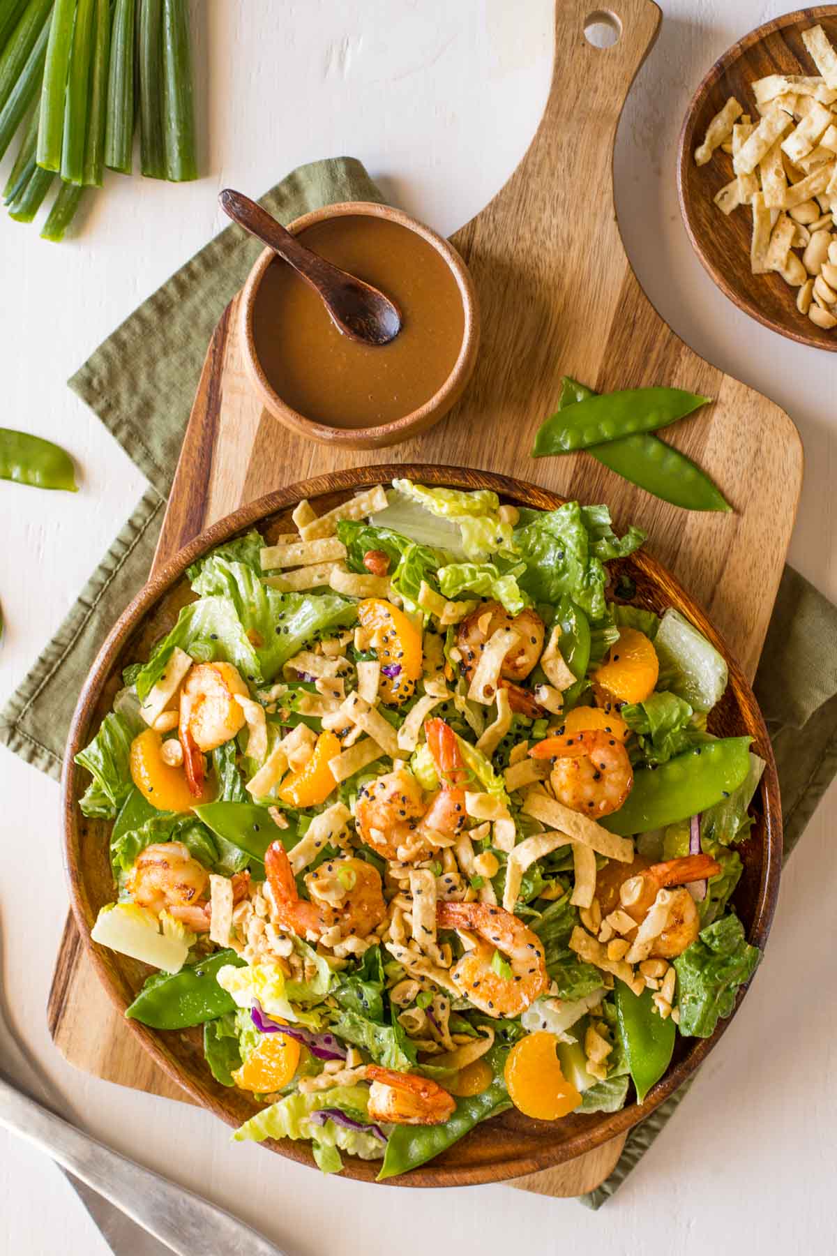 Shrimp Salad on a large serving plate, sitting next to a small wood bowl of the Spicy Peanut Dressing and a bowl of crispy wonton strips and peanuts. 