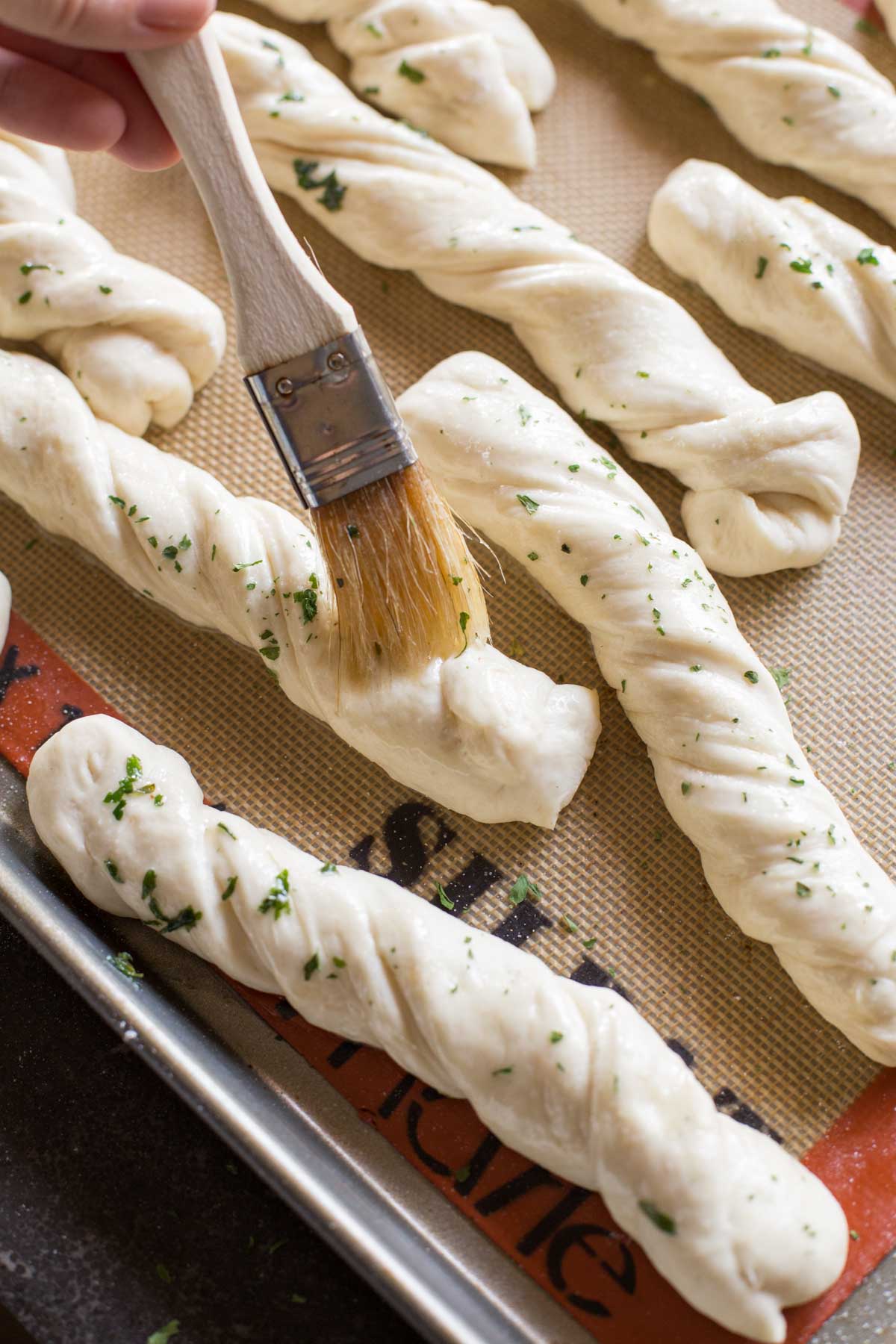 Fresh Buttery Garlic Breadsticks dough on baking sheet brushed with garlic butter.