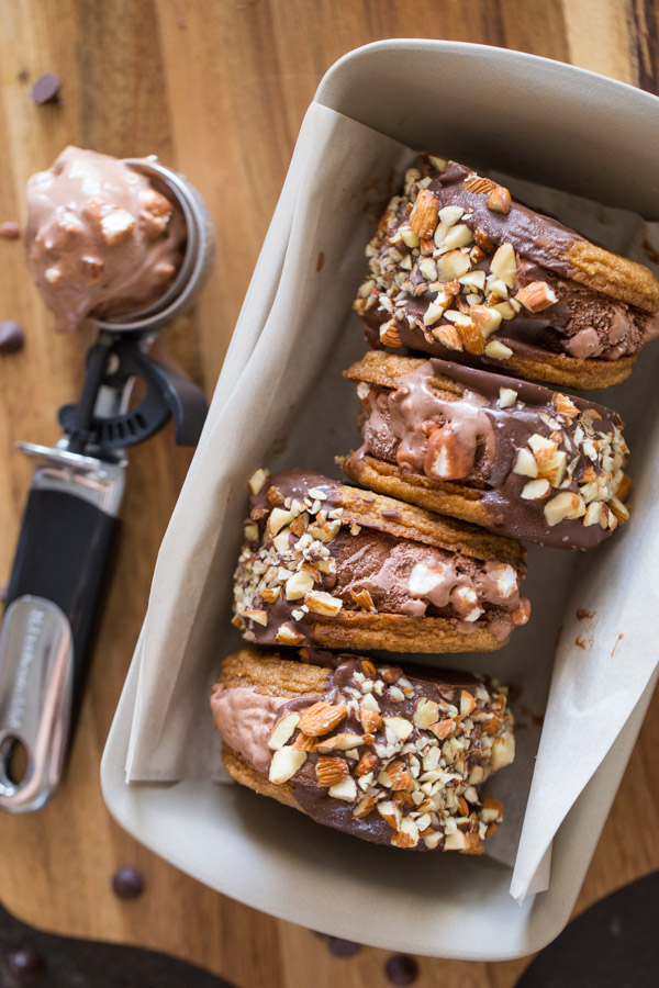Four S’more Inspired Ice Cream Sandwiches in a loaf pan, with an ice cream scooper full of Rocky Road Ice Cream sitting next to the loaf pan.