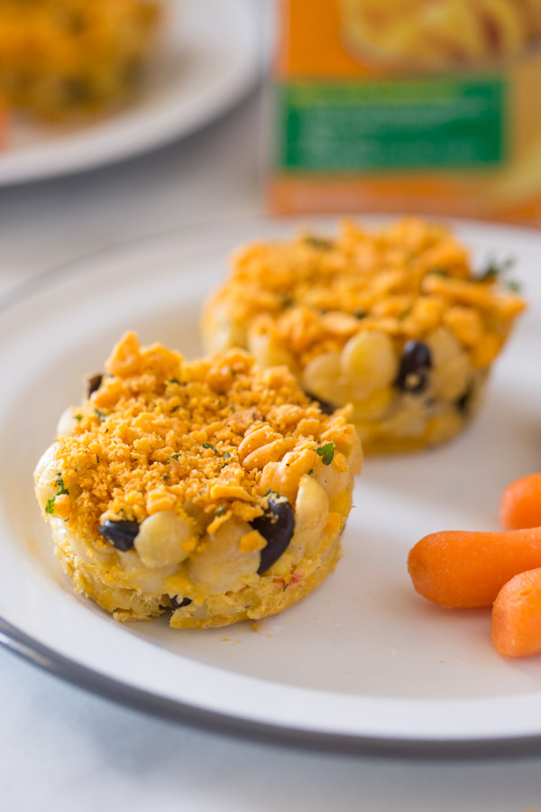 Two Southwestern Mac and Cheese cups on a plate with some carrot sticks. 
