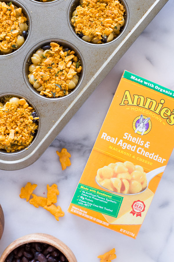 Southwestern Mac and Cheese cups in a muffin pan, sitting next to a box of Annie's Shells & Real Aged Cheddar Macaroni & Cheese. 