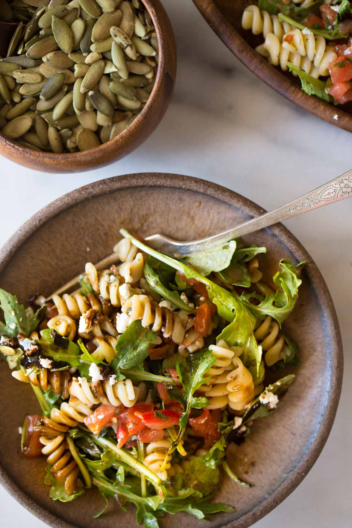 Bruschetta Pasta Salad on a plate with a fork, next to a small bowl of pepitas.