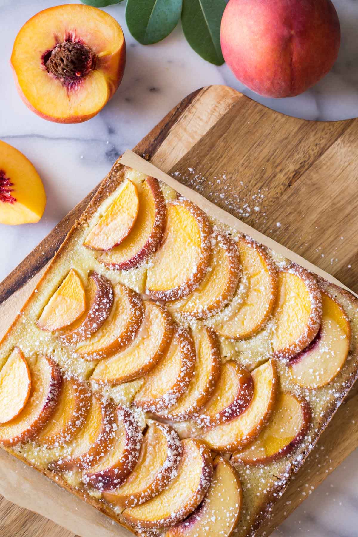 Peaches and Cream Shortbread Bars on a cutting board, with whole and cut peaches next to the board. 