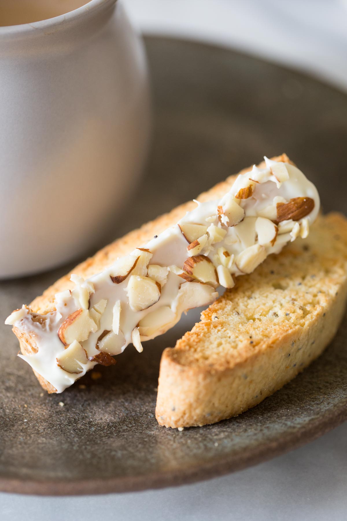 Two Almond Poppy Seed Biscotti slices on a plate, along with a cup of coffee. 