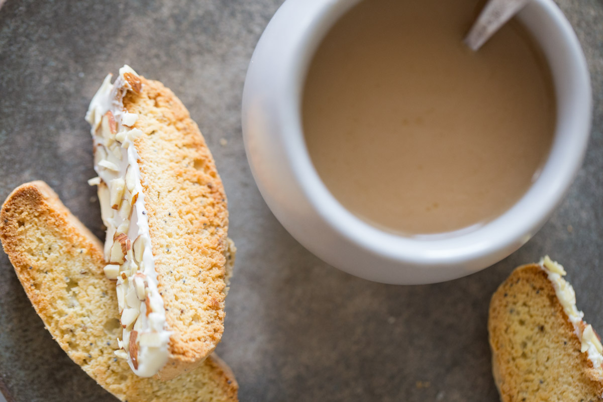 Three Almond Poppy Seed Biscotti slices on a plate, along with a cup of coffee. 