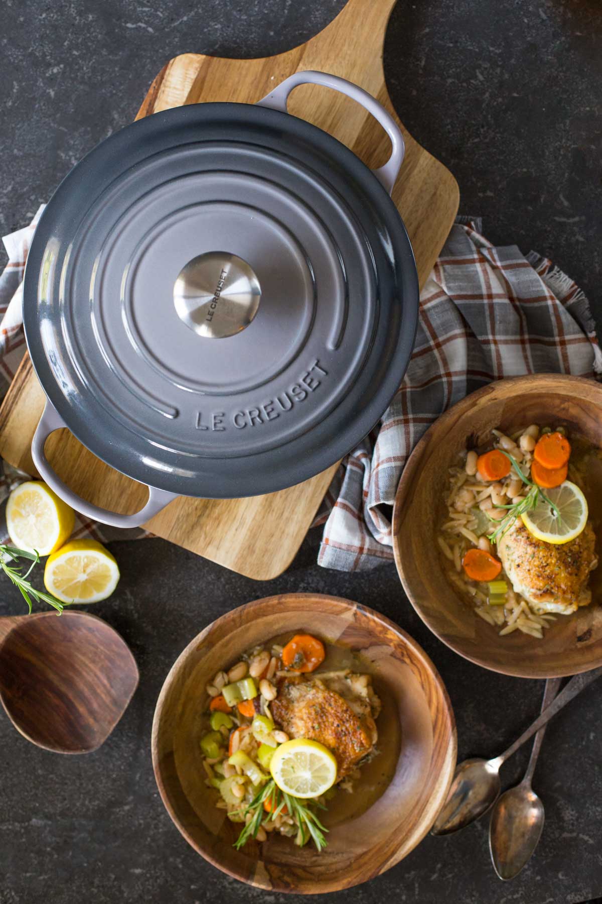 Rustic Lemon Rosemary Chicken and Orzo dished into two wood bowls, sitting next to a Le Creuset Dutch oven with the lid on. 