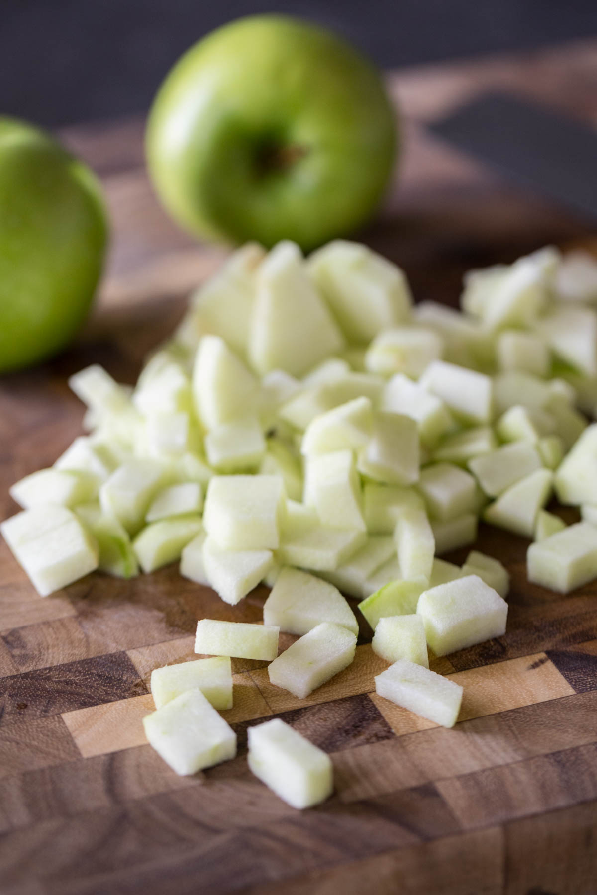 Peeled and chopped Granny Smith apples on a cutting board, with whole apples in the background. 