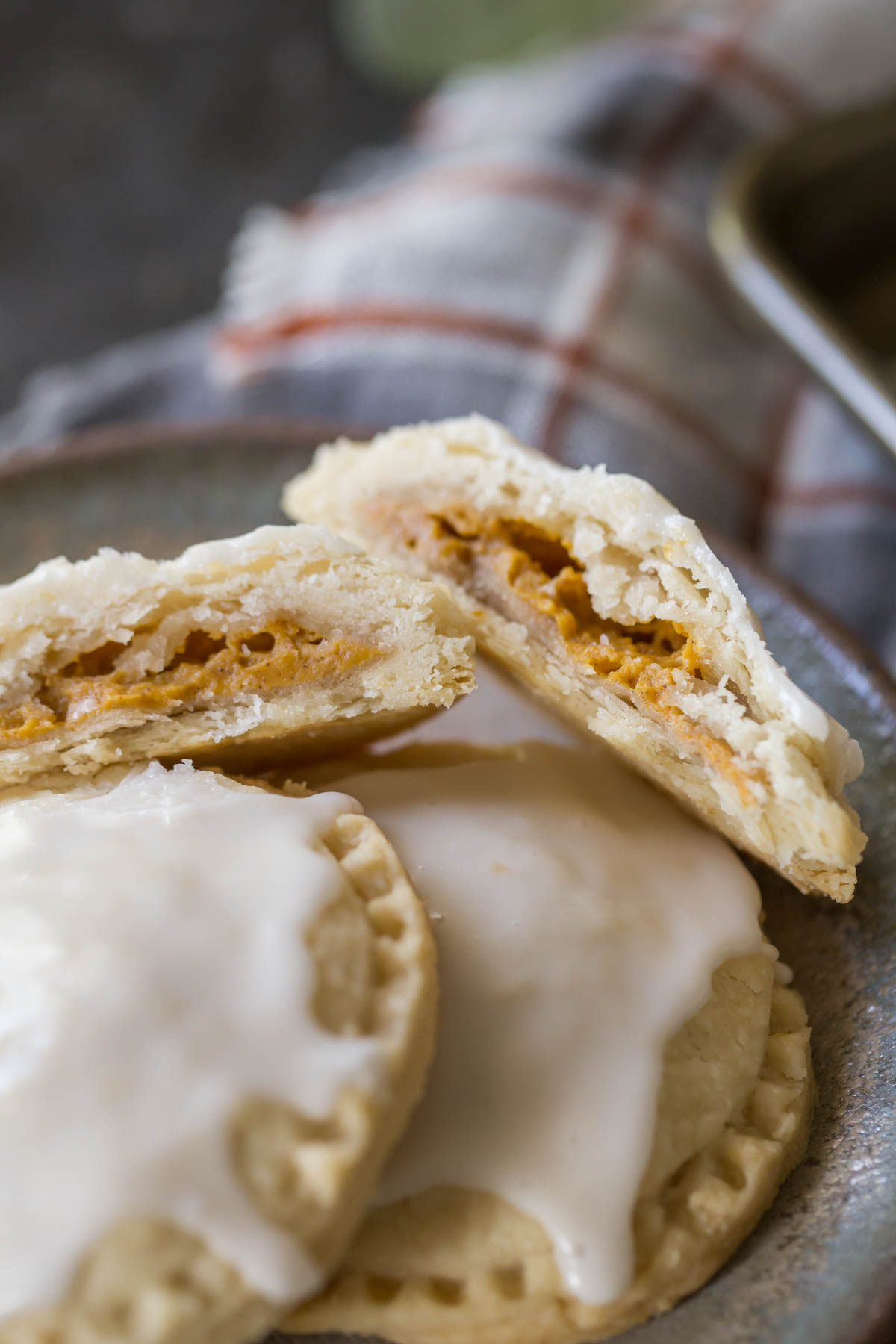 A Glazed Pumpkin Hand Pie broken in half, sitting on a plate with two whole Glazed Pumpkin Hand Pies. 