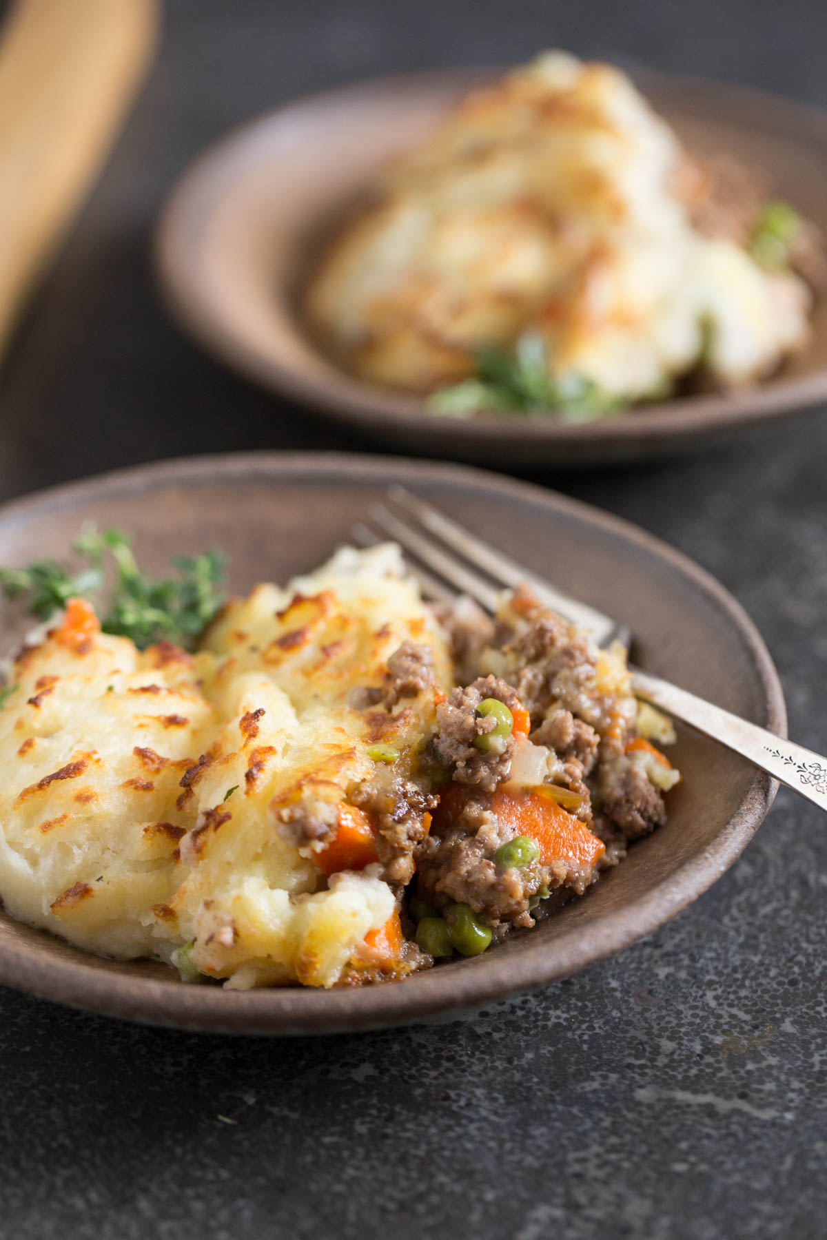 Easy Homemade Shepherd's Pie on a plate with a fork, with another serving of Easy Homemade Shepherd's Pie on a plate in the background. 