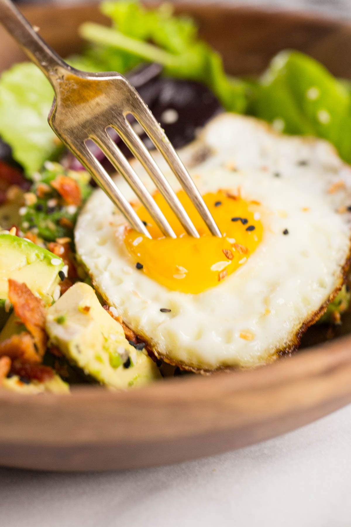 Avocado Breakfast Bowl in a wood bowl with a fork poking into the egg yolk.  