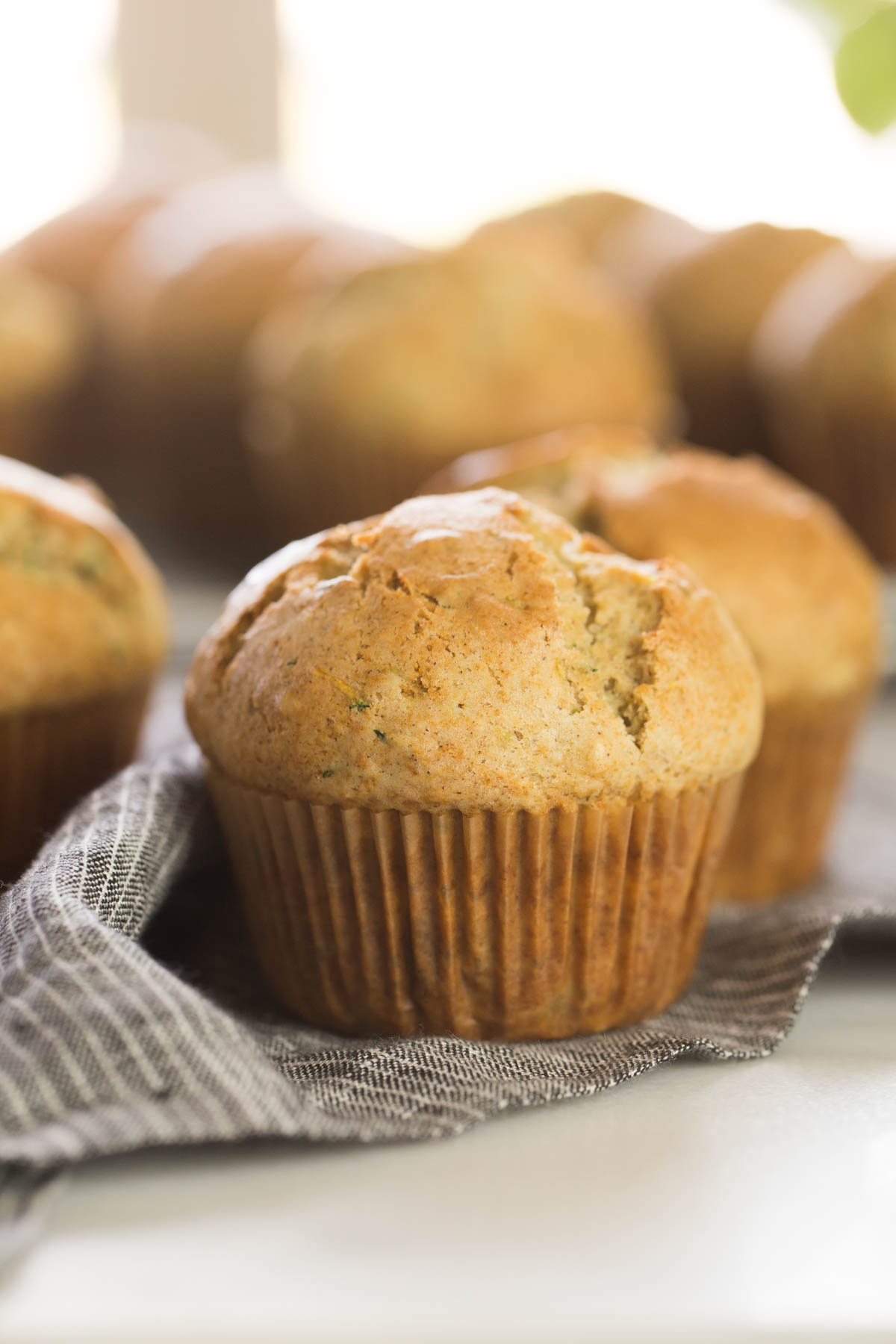 Three Healthier Zucchini Muffins on a cloth napkin, with more muffins in the background. 