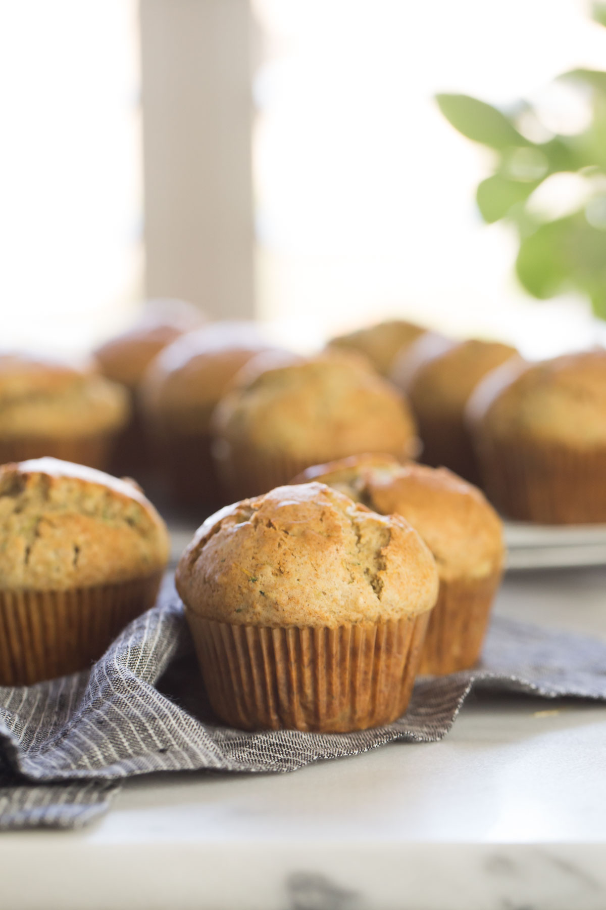 Three Healthier Zucchini Muffins on a cloth napkin, with more muffins in the background. 