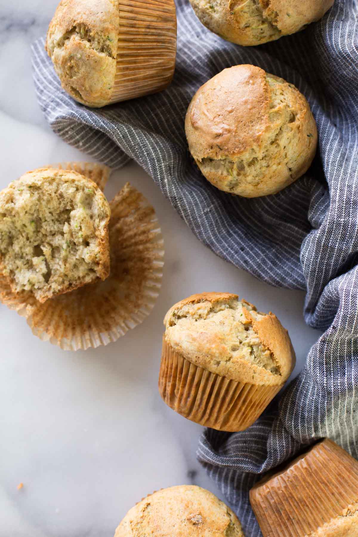 A half of a Healthier Zucchini Muffin sitting on its wrapper, with more whole muffins around it.  