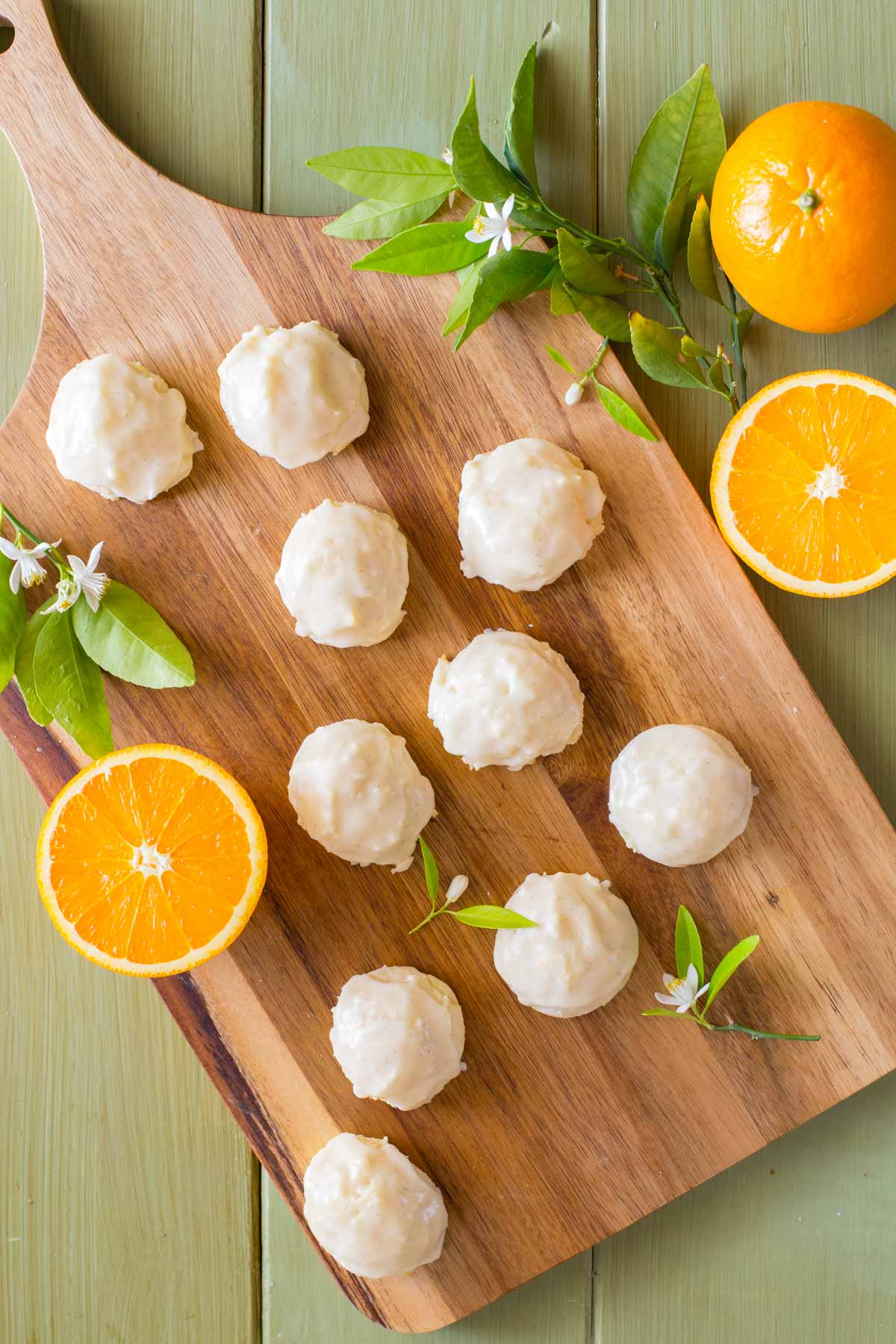 Orange Ricotta Cookies and sliced oranges with orange blossoms shot from above on a wooden cutting board. 