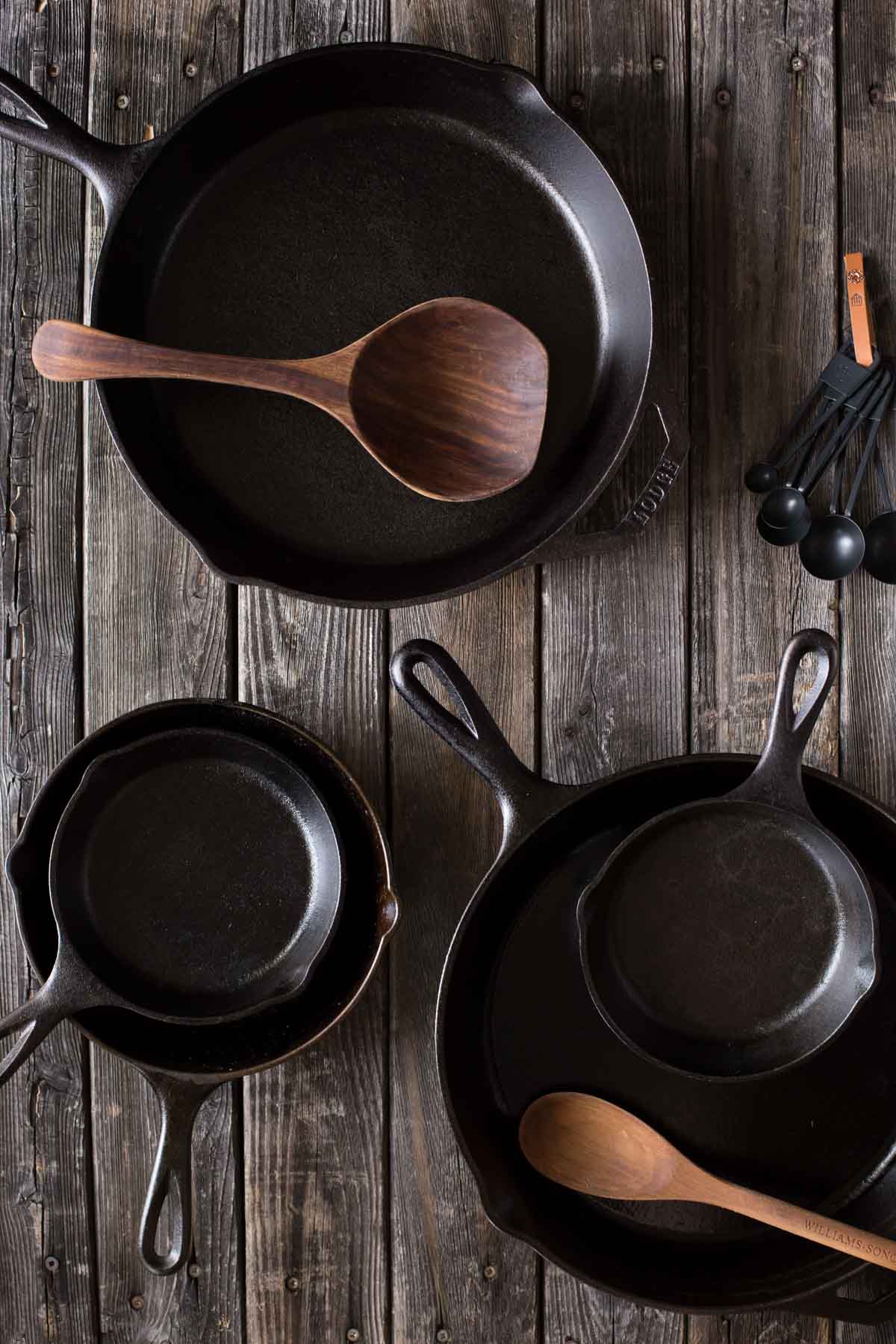 A top down view of various sizes of cast iron skillets with wooden spoons. 