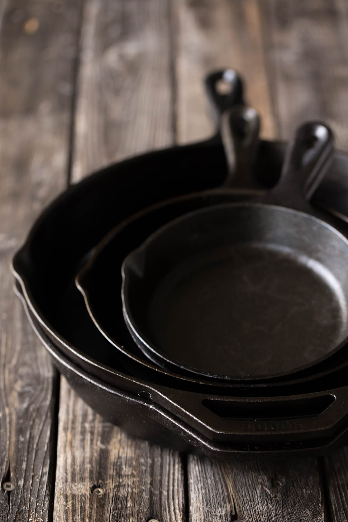 Five cast iron skillets stacked on a wooden board. 