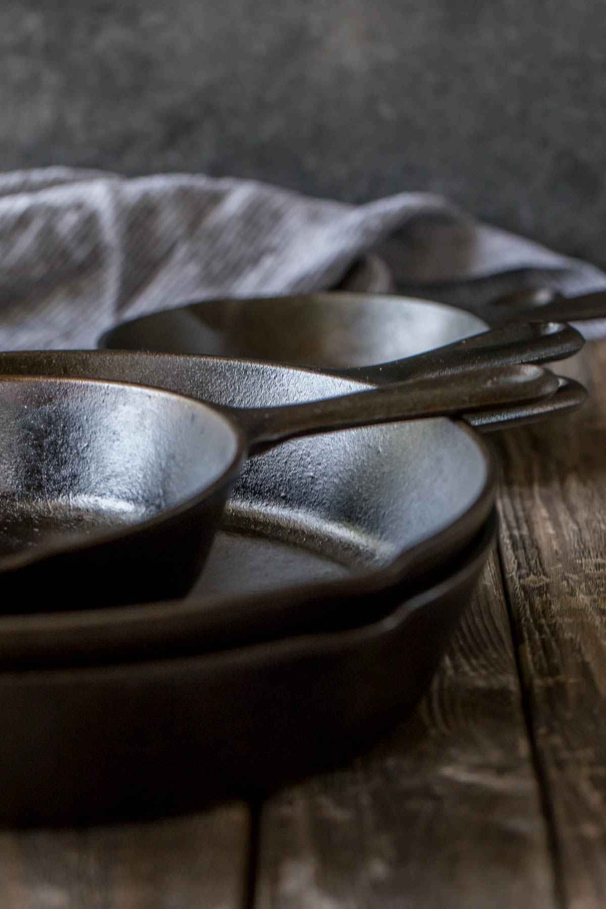Five cast iron skillets stacked on a wooden board, with a dish cloth in background.