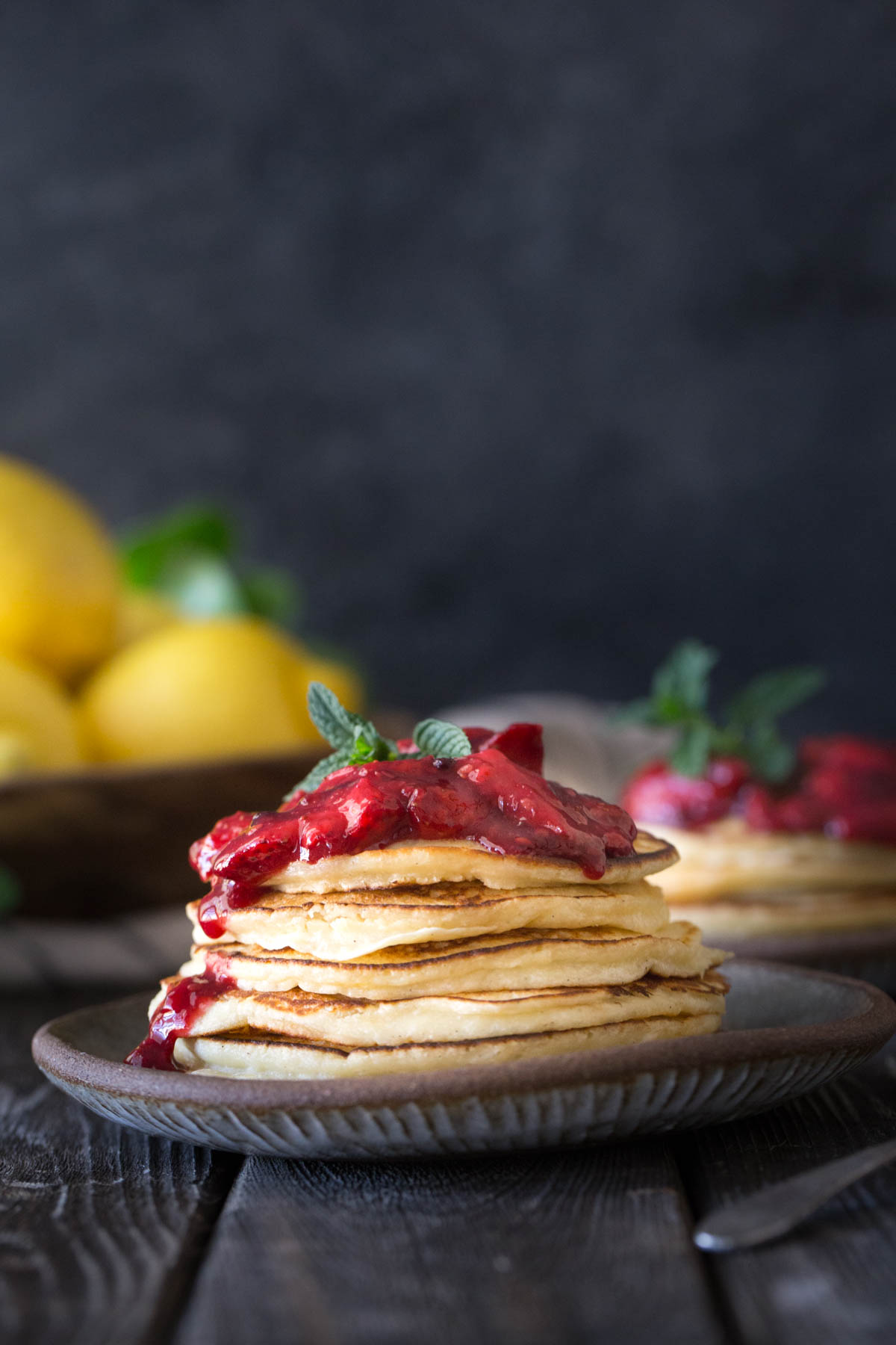 A stack of Lemon Ricotta pancakes with fresh berry sauce on a grey background. 