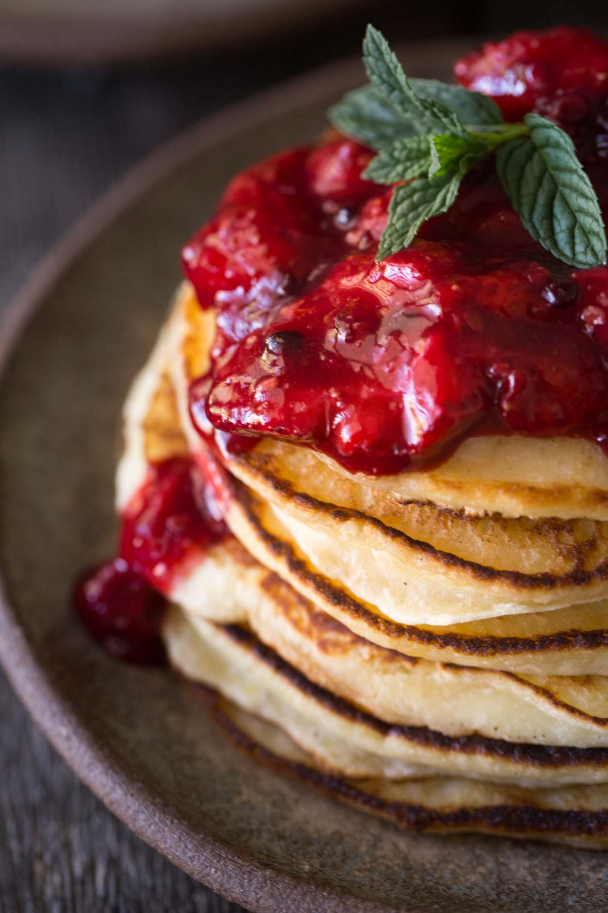 Stack of pancakes with fresh berry sauce on top and a sprig of mint. 