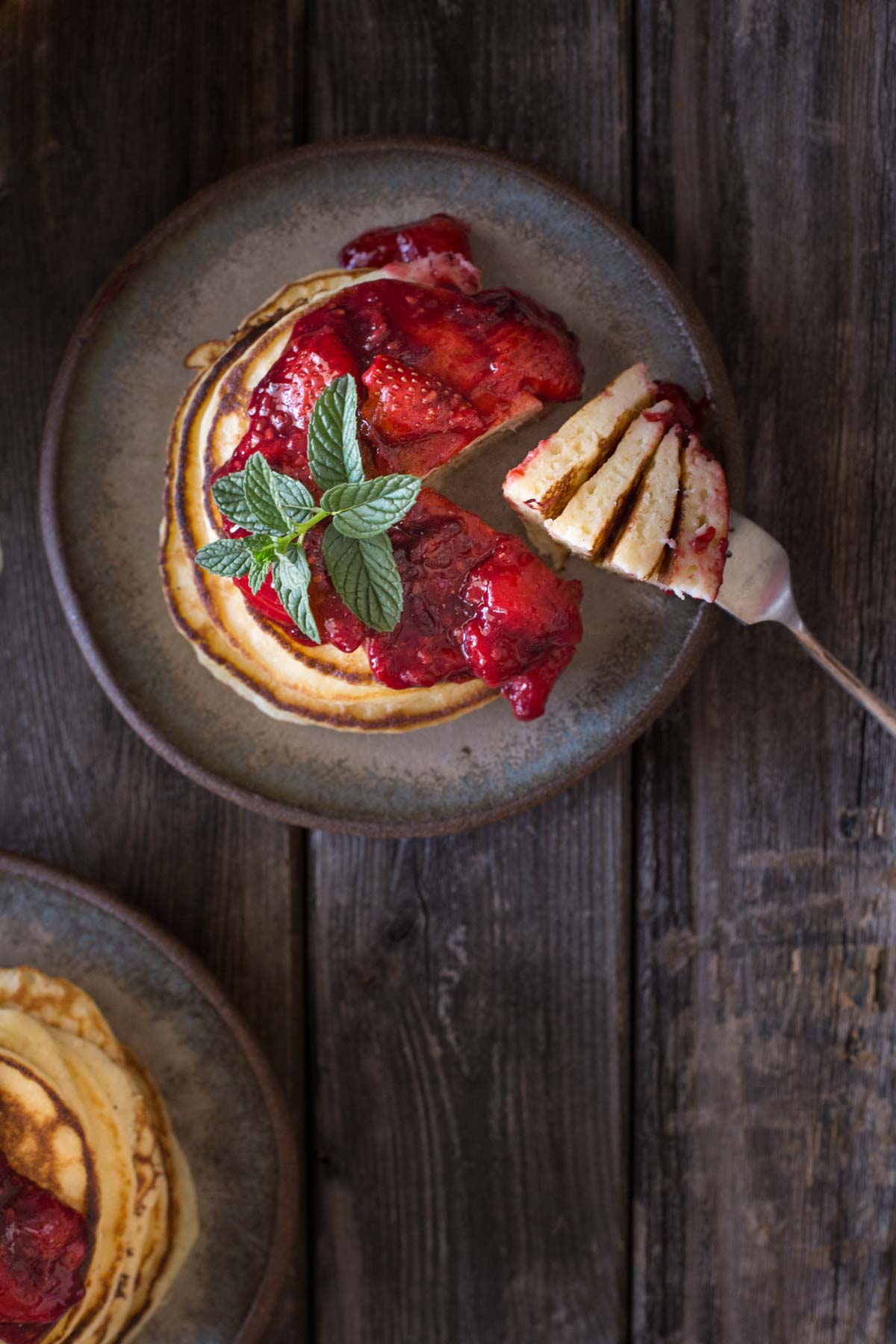 A top down view of a stack of lemon ricotta pancakes with fresh berry sauce. 