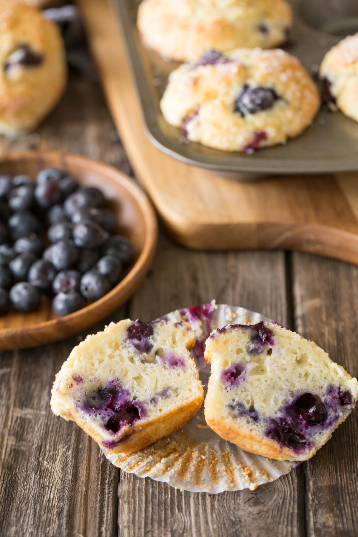 Best Ever Buttermilk Blueberry Muffins in a muffin pan with a muffin cut in half in the front of the picture. 