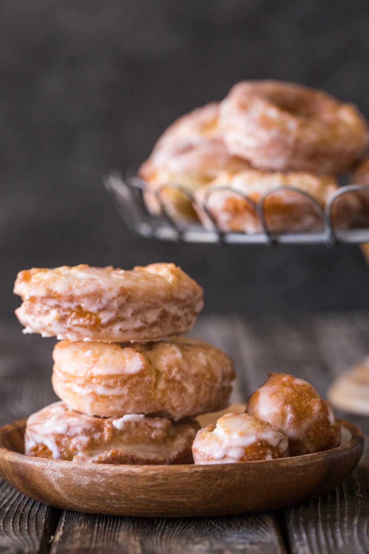 Stack of three Old Fashioned Buttermilk Donuts from the front view with a cake plate holding donuts in the background. 