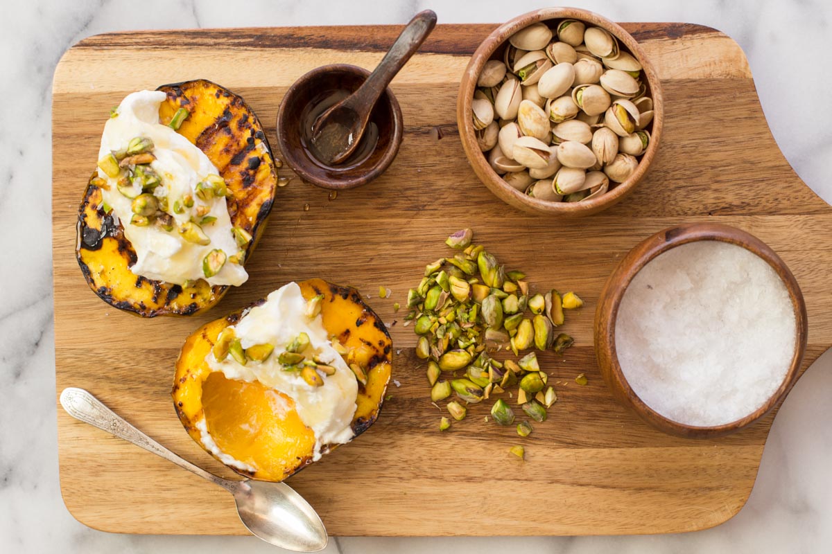 Overhead shot of wooden board with Grilled Mango With Honey Ricotta Whipped Cream, sea salt, honey, and pistachios
