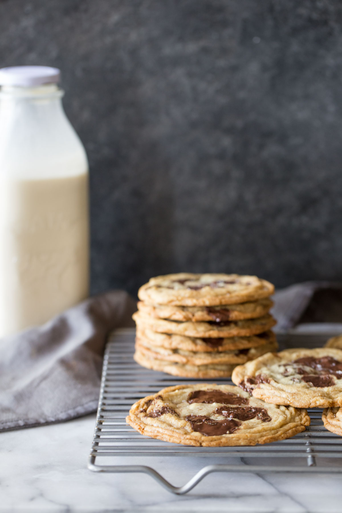 Toffee Almond Chocolate Chunk Cookies on a cooling rack with a bottle of milk in the background. 