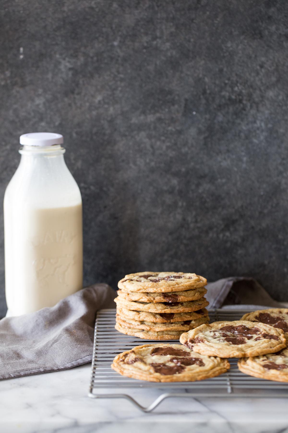 Toffee Almond Chocolate Chunk Cookies on a cooling rack with a bottle of milk in the background. 