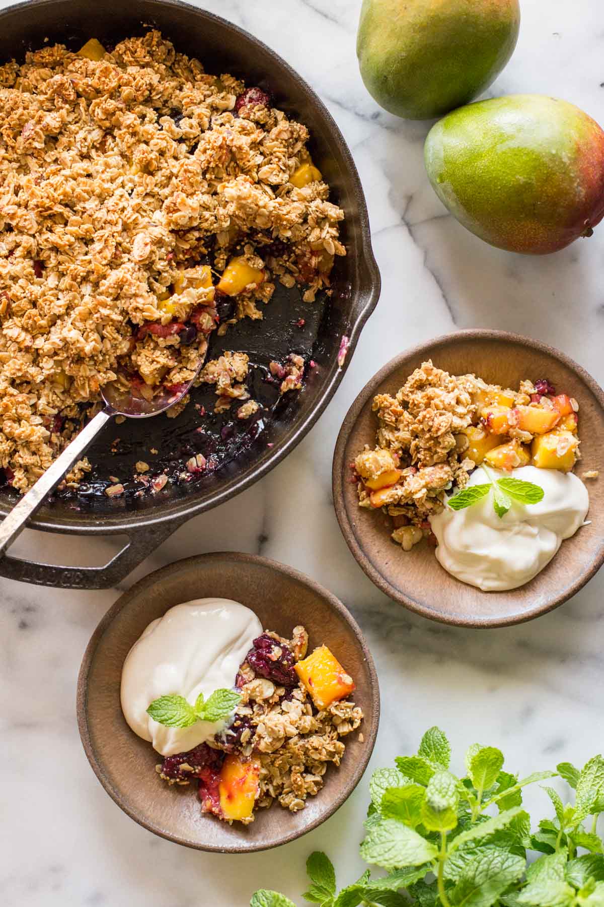 Mango Berry Breakfast Crisp in a cast iron skillet, with two bowls ready to serve. 
