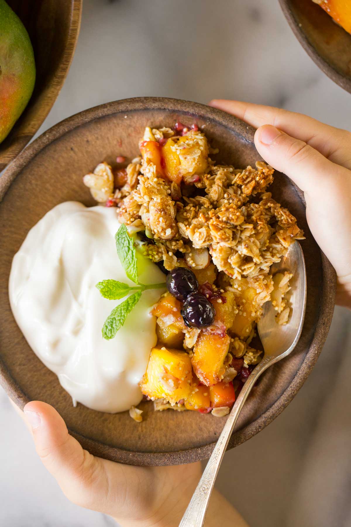 Mango Berry Breakfast Crisp on in a bowl with a side of yogurt. 
