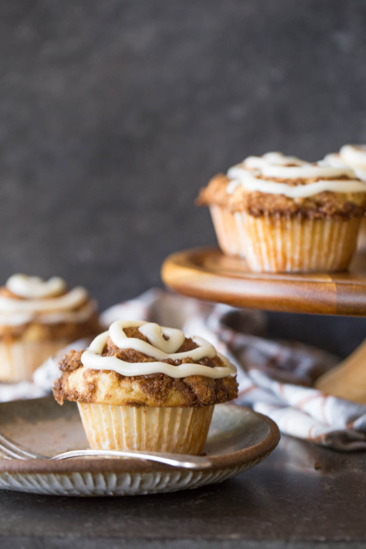 Cinnamon Roll Muffins with a cream cheese icing swirl on a grey plate with a fork. 