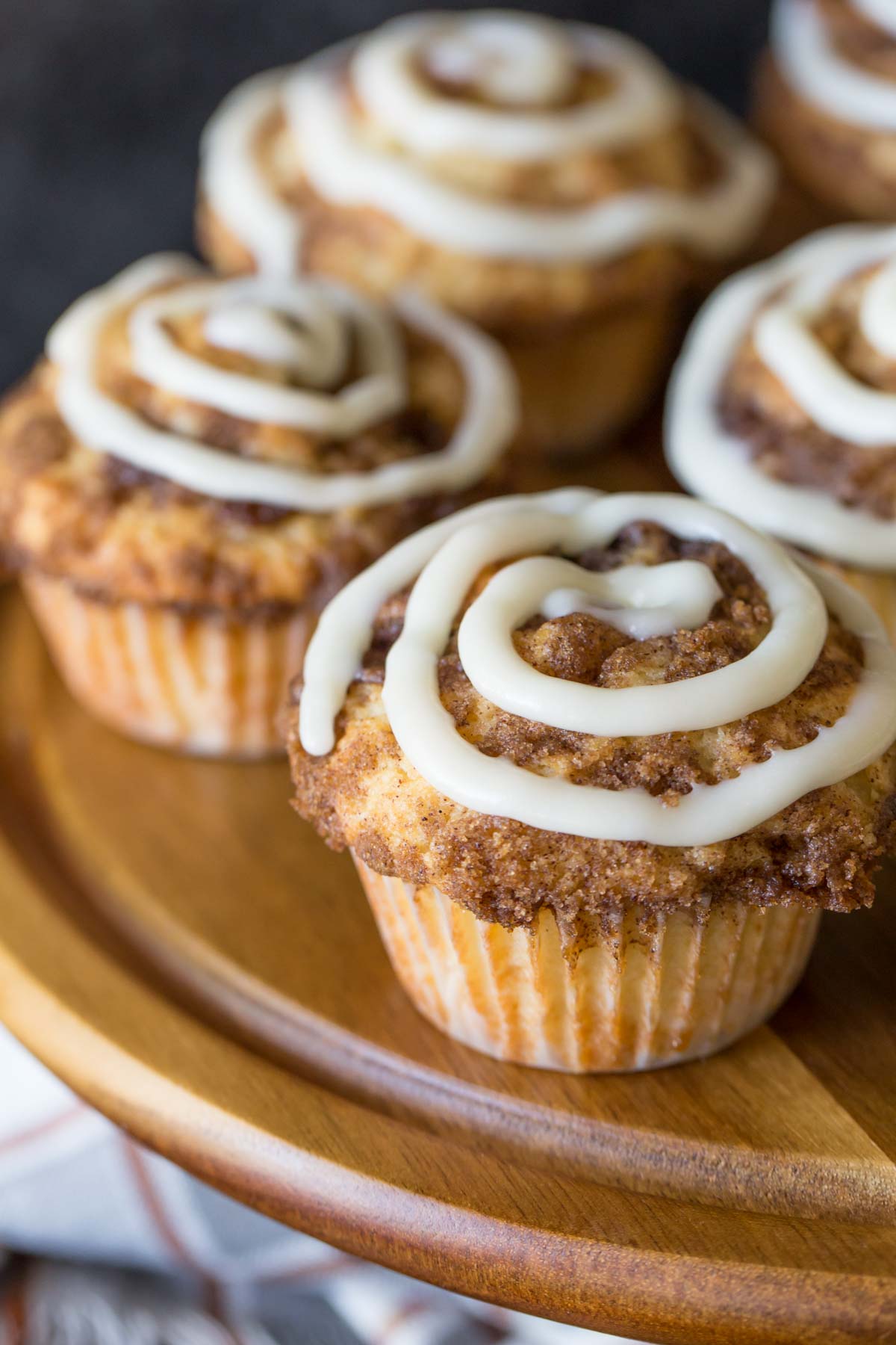 Cinnamon Roll Muffins with a cream cheese icing swirl on a wooden cake stand.